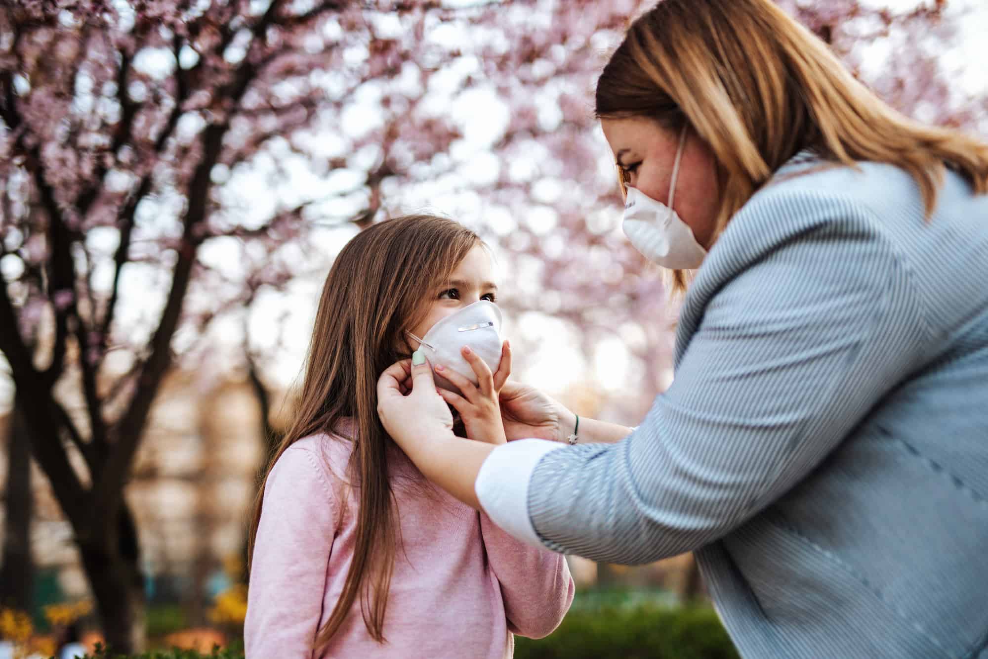 Mother placing protective mask on face of her daughter. Coronavirus, Covid-19 concept.